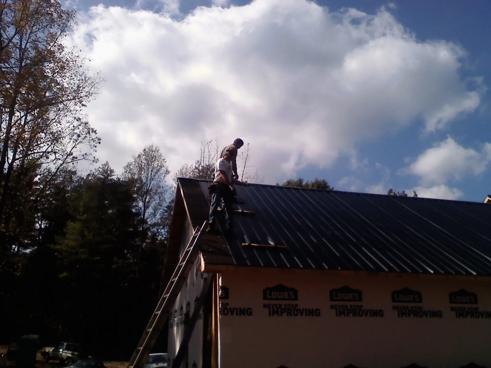 Roofer fastening dark metal panels high against a cloudy sky, from a Roof Inspection job in Oak Forest